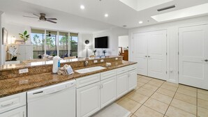 A spacious kitchen with granite countertops, white cabinetry, a built-in dishwasher, and a large window offering a view of the outdoors. - Lost Key B203 (Pensacola)