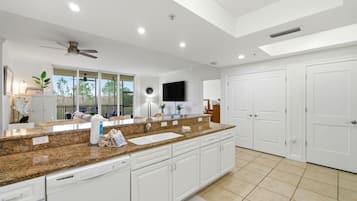 A spacious kitchen with granite countertops, white cabinetry, a built-in dishwasher, and a large window offering a view of the outdoors.