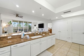 A spacious kitchen with granite countertops, white cabinetry, a built-in dishwasher, and a large window offering a view of the outdoors. - Lost Key B203 (Pensacola)