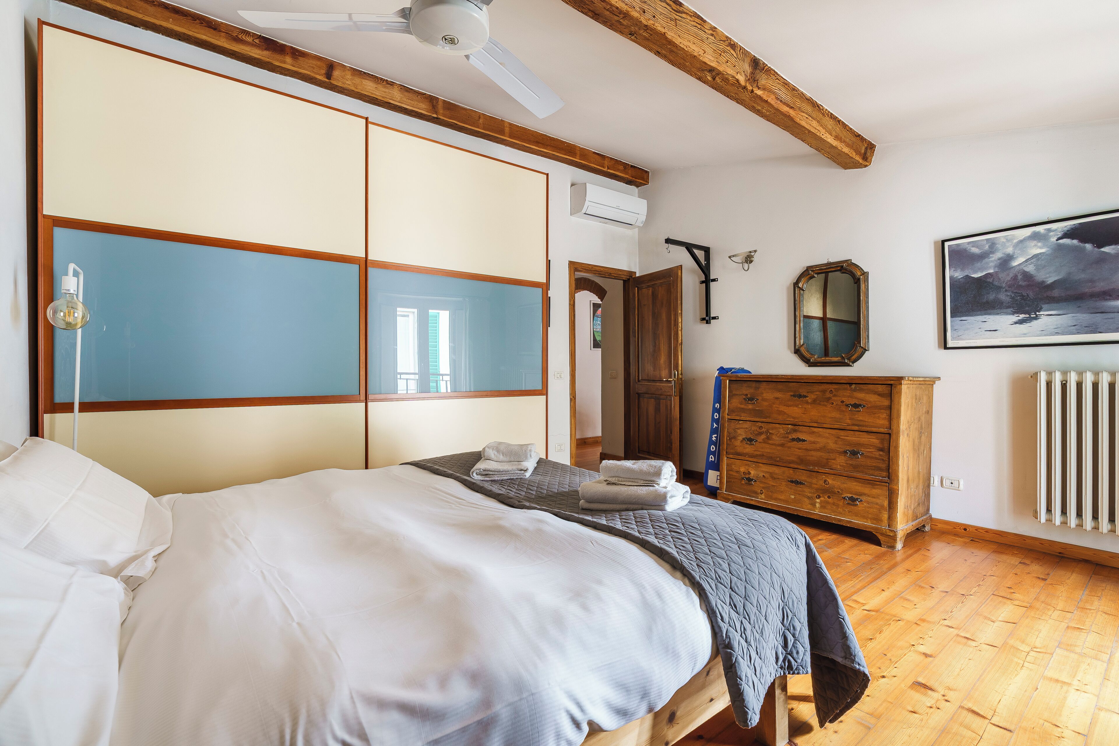 A bedroom with a bed, a dresser, a mirror, and a painting on the wall.