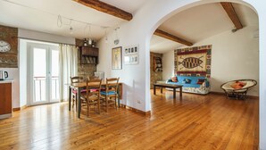 Un salón amplio con suelo de madera, una mesa de comedor con sillas, un sofá y un tapiz con motivos de peces.