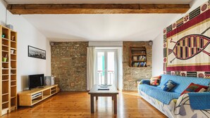 Una sala de estar con piso de madera, pared de piedra, sofá azul con cojines estampados, un mueble bajo para televisor de madera y una estantería.