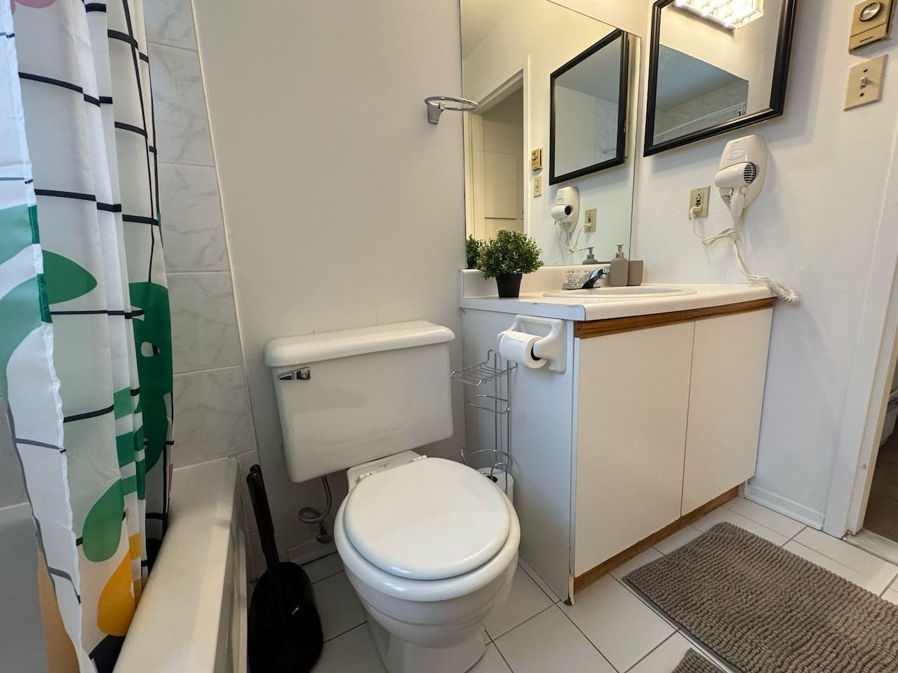 A bathroom with a toilet, sink, mirrors, and a shower curtain.