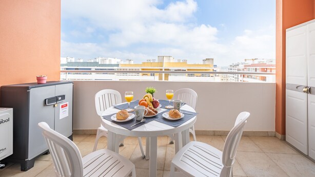 A balcony with a table set for breakfast, chairs, a refrigerator, and a view of buildings. - Studio Aqua with Shared Pool, WiFi and Air Conditioning (Portimão)