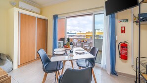A dining area with a table set for two, a fire extinguisher, and a view of the cityscape through the window. - Studio Aqua with Shared Pool, WiFi and Air Conditioning (Portimão)