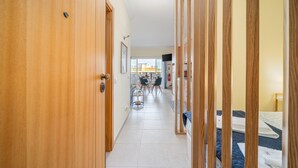 A hallway with wooden doors, a dining area with chairs and a table, and a bed with neatly folded towels. - Studio Aqua with Shared Pool, WiFi and Air Conditioning (Portimão)