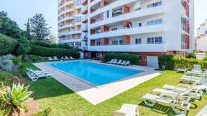 A multi-story hotel with a swimming pool surrounded by lawn chairs and a well-maintained garden. - Studio Aqua with Shared Pool, WiFi and Air Conditioning (Portimão)