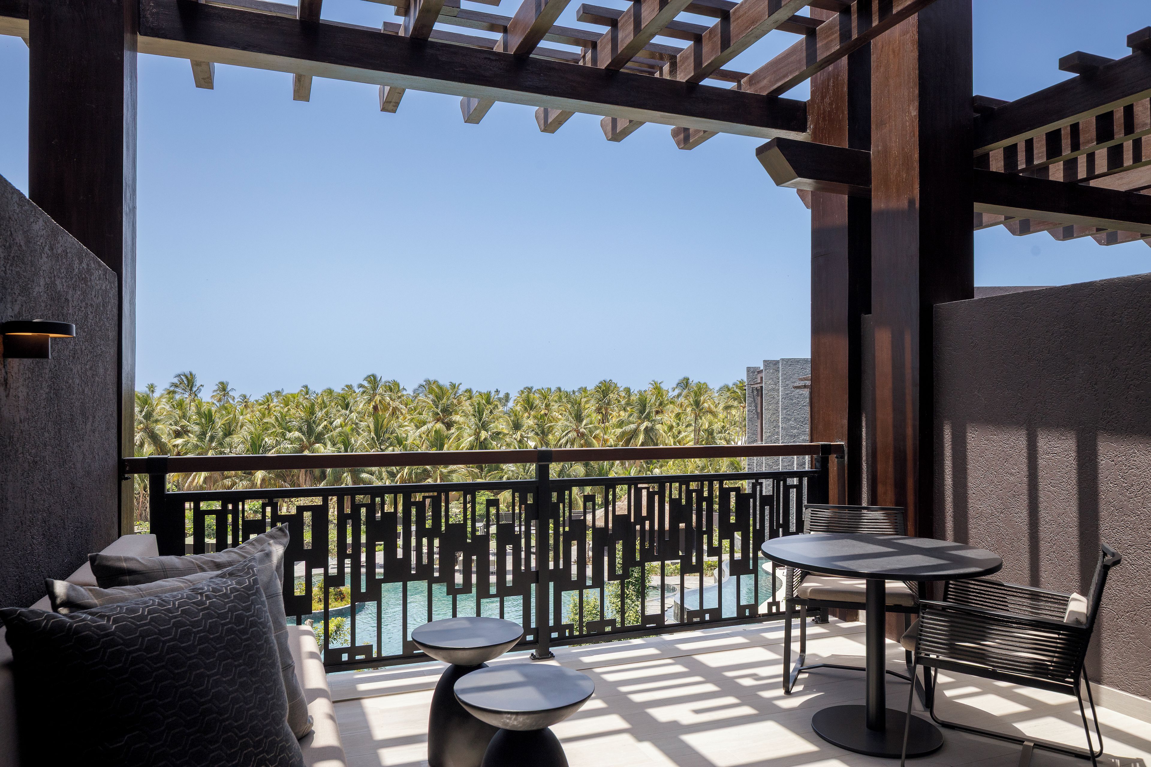 Un balcon avec vue sur les palmiers et une piscine, aménagé avec une table et des chaises.