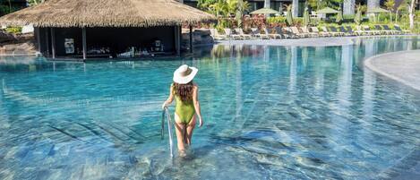A clear pool with a person in a swimsuit and a hat walking towards the edge.