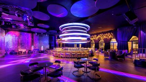 A modern bar area with a circular seating arrangement, ambient lighting, and a stage for performances. - Lopesan Serenity Bay Resort, Spa & Casino – Adults Only All-Inclusive (Punta Cana)