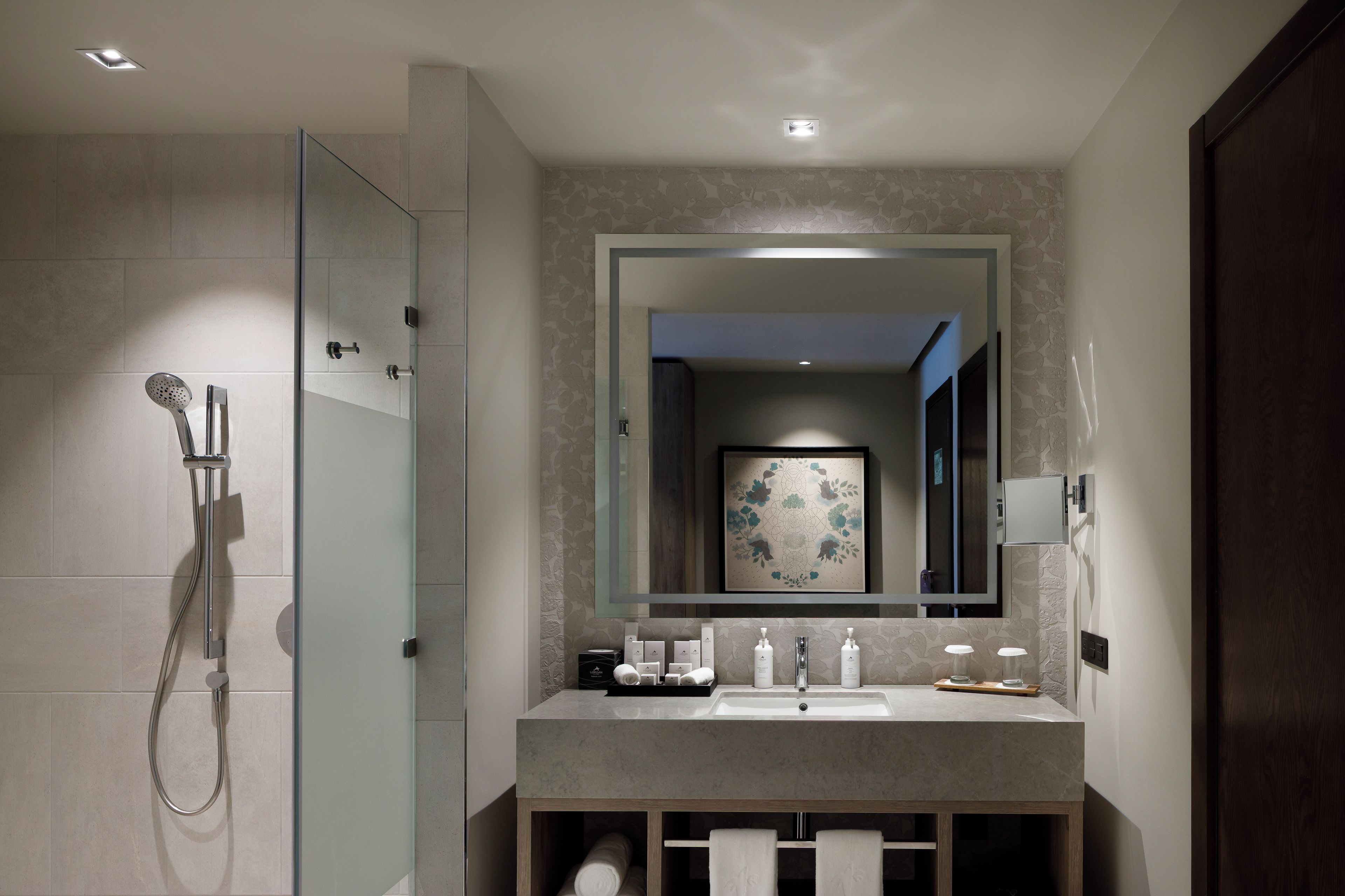 Un baño moderno con ducha envuelta en vidrio, un espejo grande y un tocador con lavabo y artículos de aseo.