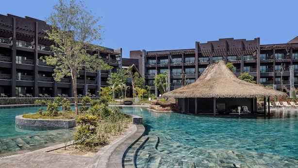 A hotel with a swimming pool, a thatched-roof structure, and a multi-story building with balconies. - Lopesan Serenity Bay Resort, Spa & Casino – Adults Only All-Inclusive (Punta Cana)