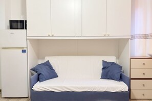 Una stanza compatta con un letto, un frigorifero bianco e un angolo cottura.
