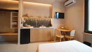 A compact kitchen with a built-in stove, a small refrigerator, and a microwave. There is a dining area with a table and two chairs. A flat-screen TV is mounted on the wall above the dining table. - Essenza Boutique Apartments (Cefalù)