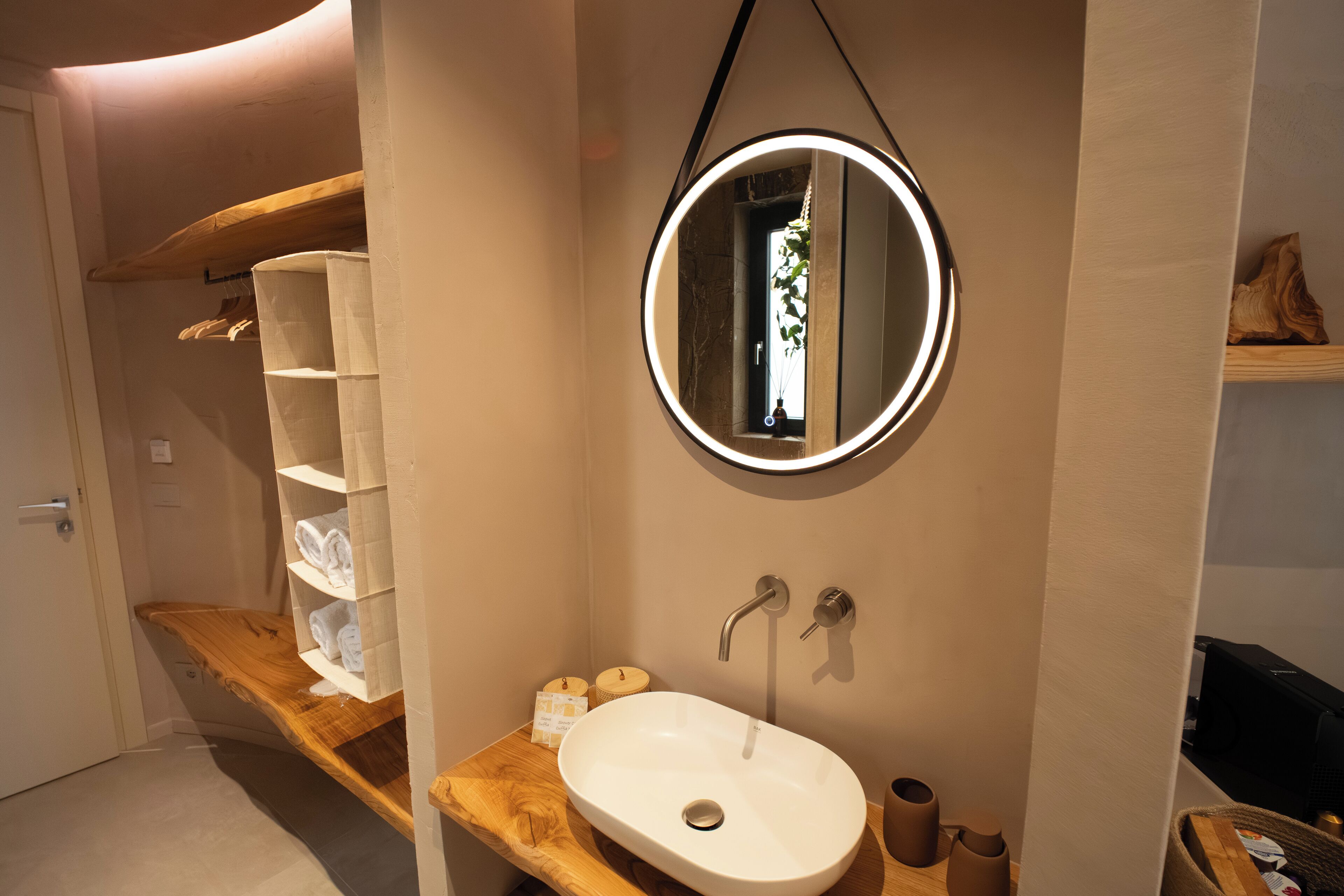 Un baño moderno con tocador de madera, espejo redondo y lavamanos blanco.