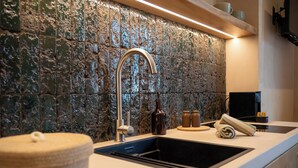 A kitchen with a stone backsplash, a modern faucet, and a countertop with a sink. - Essenza Boutique Apartments (Cefalù)