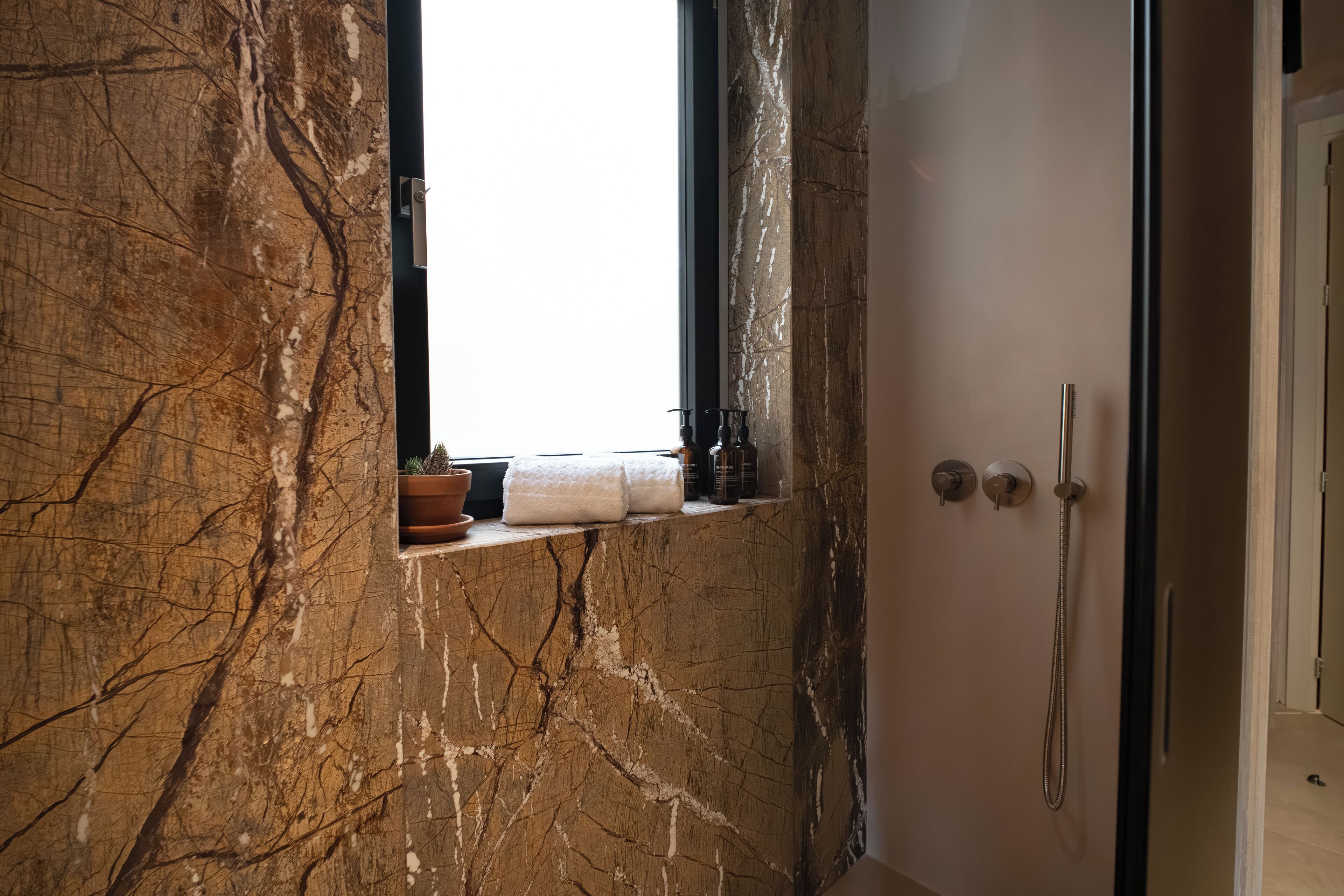 A bathroom with a marble wall, a window, a towel rack, and a shower.