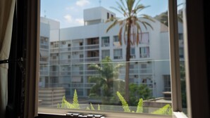 A view through a window with a clear sky, a palm tree, and a building with balconies. - Essenza Boutique Apartments (Cefalù)