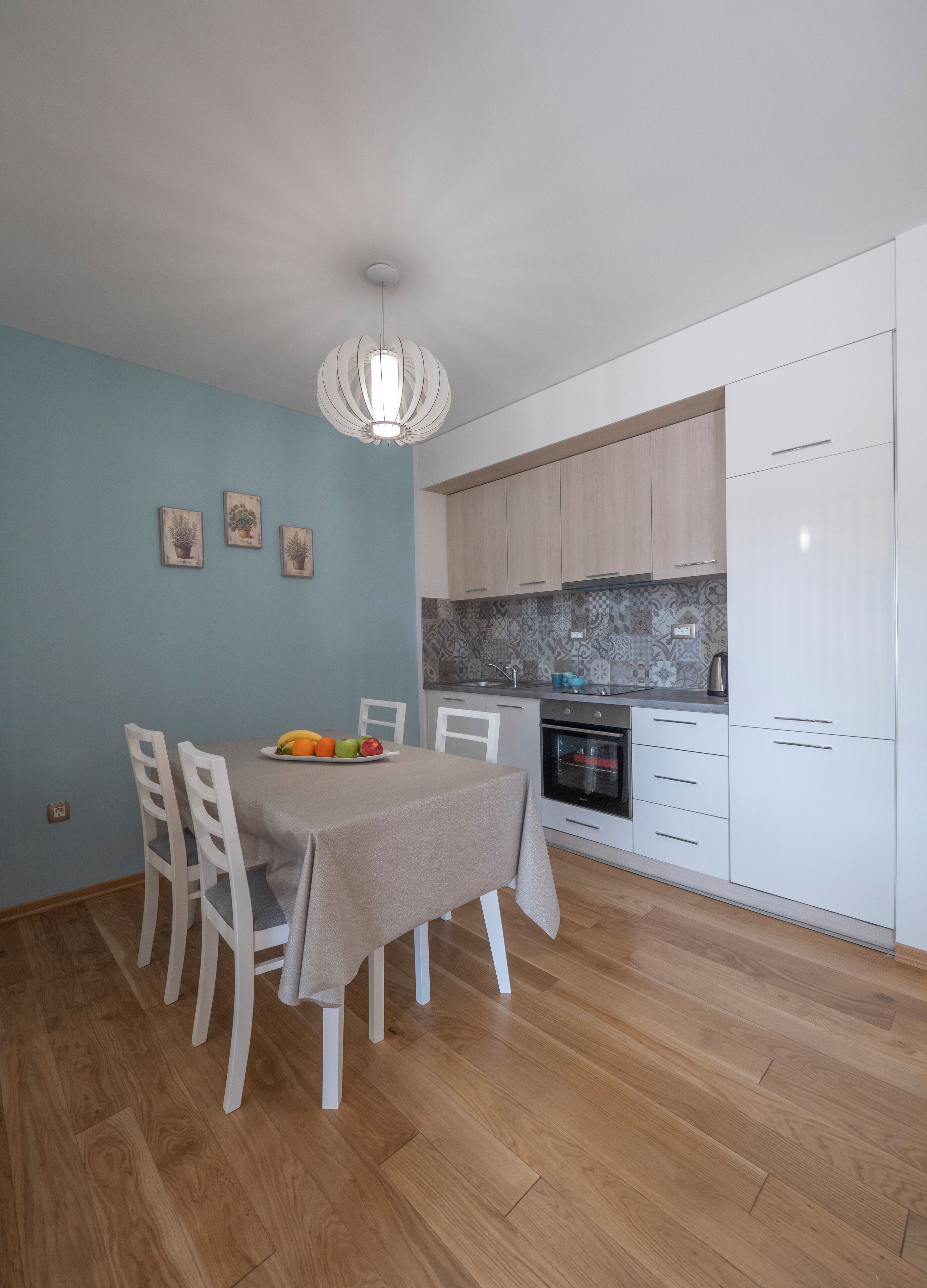 Cocina compacta con armarios blancos, horno integrado y comedor con mesa dispuesta para dos.