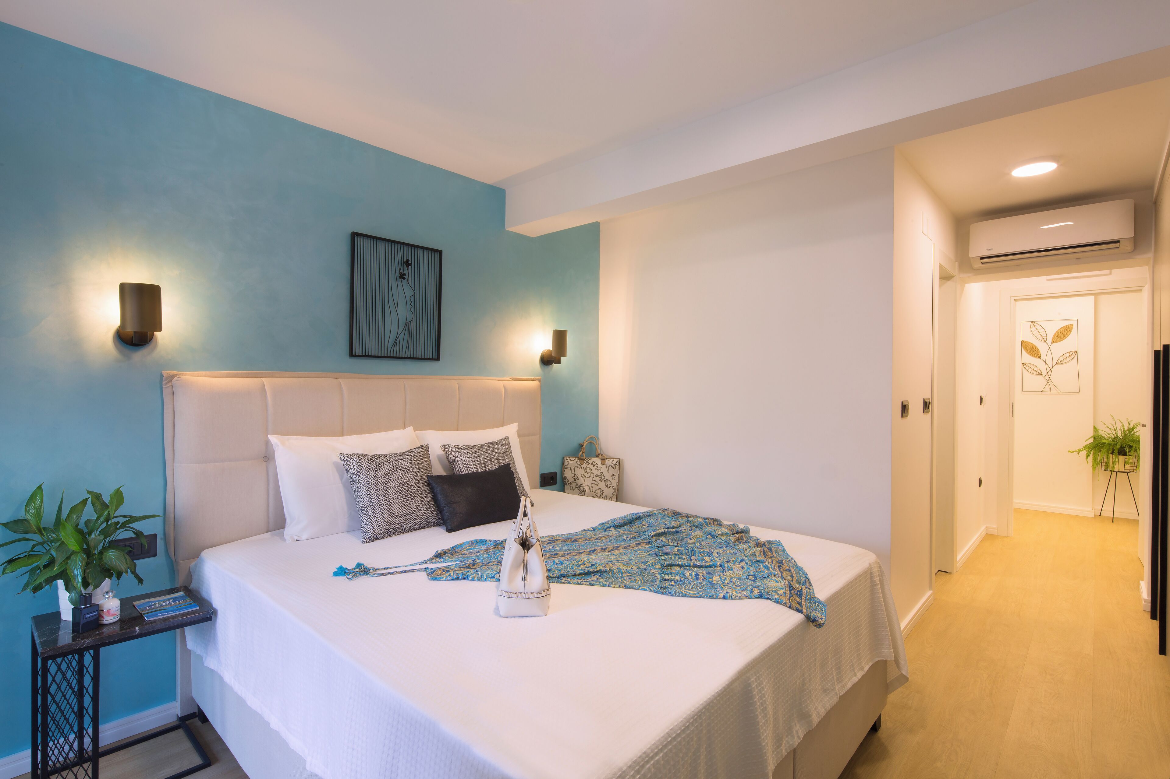 A neatly made bed with a white headboard, a bedside table with a plant, and a wall-mounted light fixture.