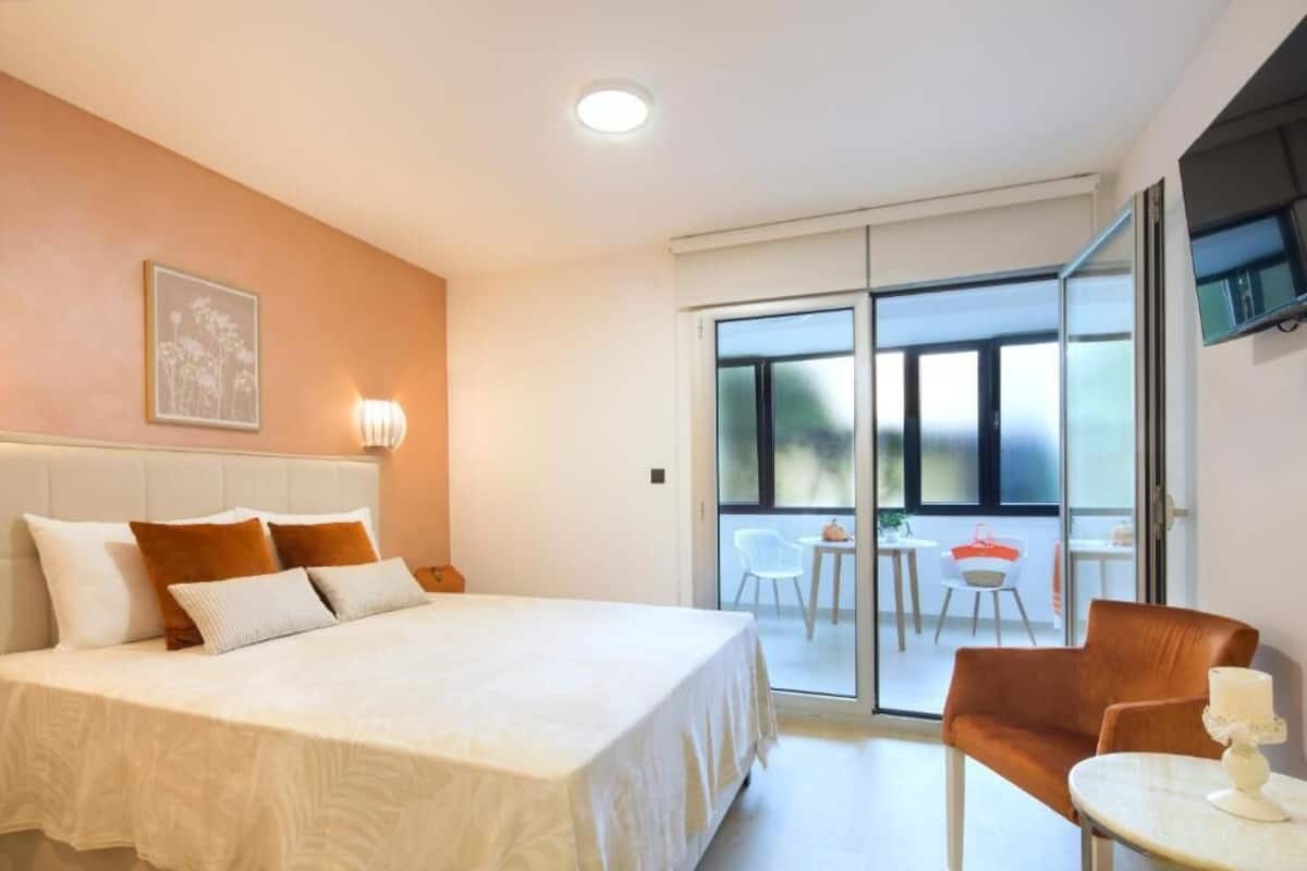 A hotel room with a large bed, a sofa, a small table, and a balcony with chairs.