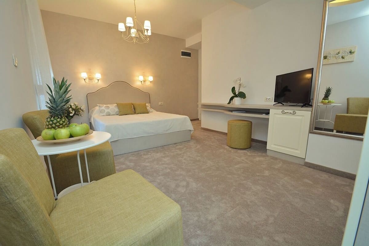 A compact hotel room with a bed, a small desk, a television, and a seating area with a table and chairs.