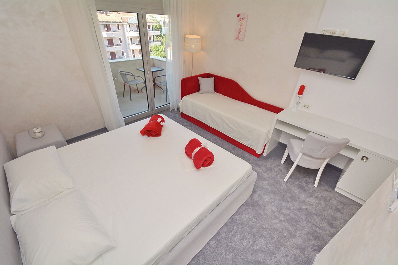 Hotellihuone, jossa on sänky, työpöytä, tuoli, televisio ja parveke, jossa on myös tuoli.