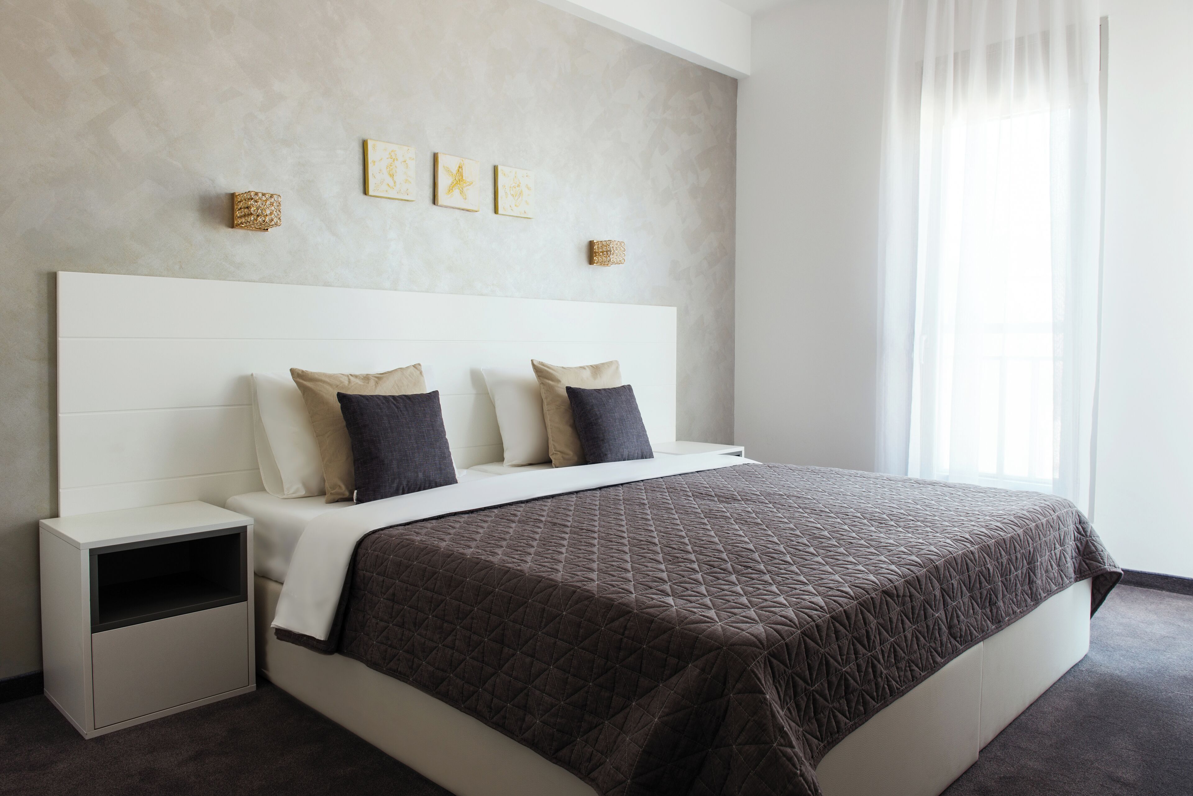 A modern bedroom with a large bed, white headboard, and a nightstand.