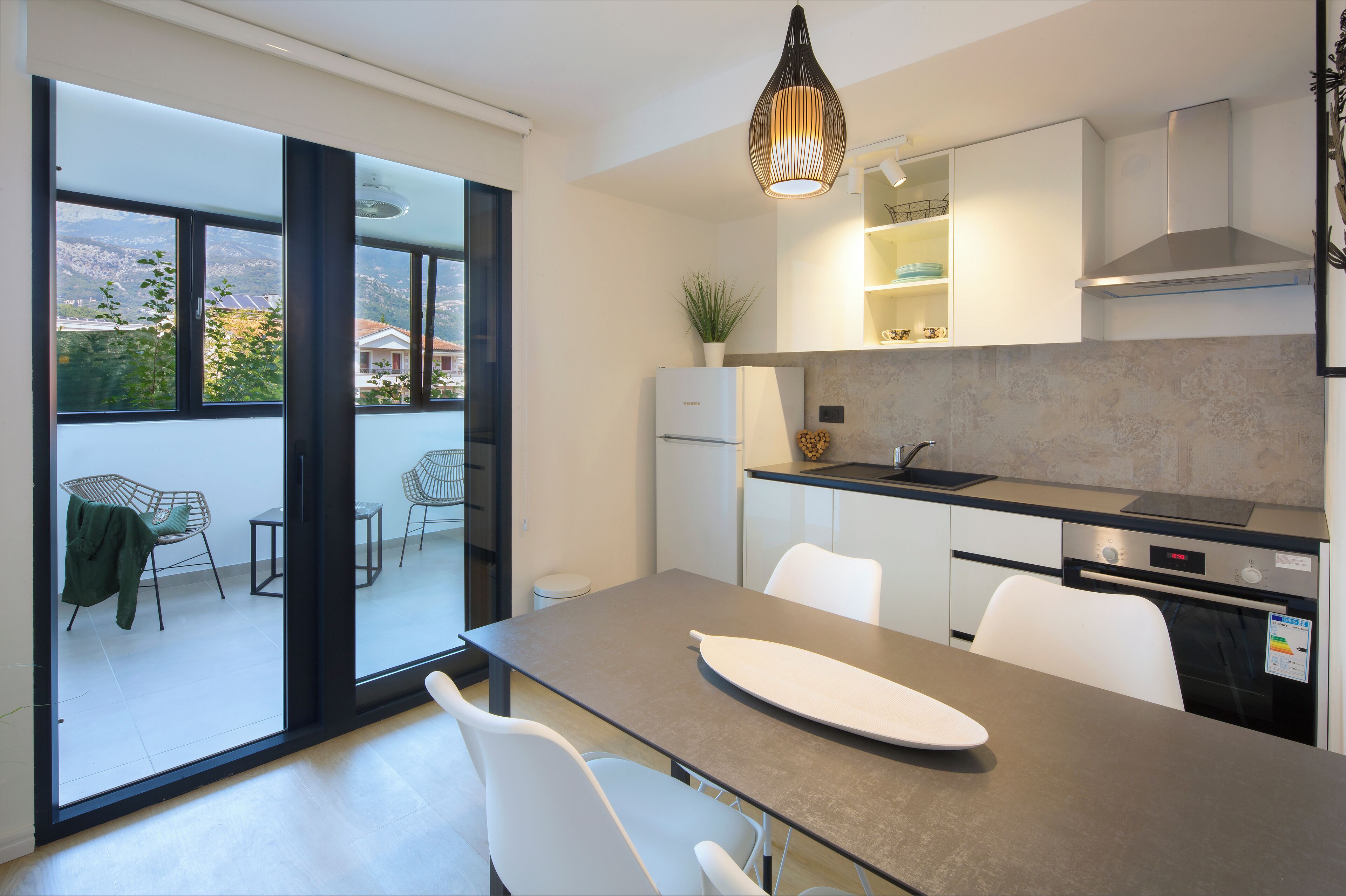 Une cuisine moderne dotée d’un grand îlot central, de meubles blancs et offrant une vue sur l’extérieur grâce à de grandes fenêtres.