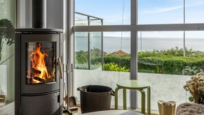 Quarto moderno com lareira a lenha, vista para área verde e edifícios, e uma grande janela.