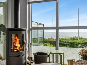 Ein modernes Zimmer mit Kaminofen, Blick auf Grünflächen und Gebäude, sowie einem großen Fenster.