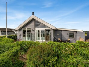 Ein modernes Haus mit großen Glasfenstern, einem markanten Schornstein und einem gepflegten Garten.