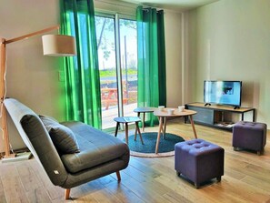 Un salon moderne comprenant un canapé, des poufs, une table basse, un téléviseur et un lampadaire.