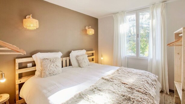 A bedroom with a wooden bed, two bedside lamps, a window with curtains, and a wooden wardrobe. - Cottage Duo Syrah Sauna Gaillac- LesCottagesduTarn (Brens)