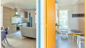 A modern kitchen with wooden cabinets, a grey sofa, and a dining area with a table and chairs. - Cottage Duo Syrah Sauna Gaillac- LesCottagesduTarn (Brens)