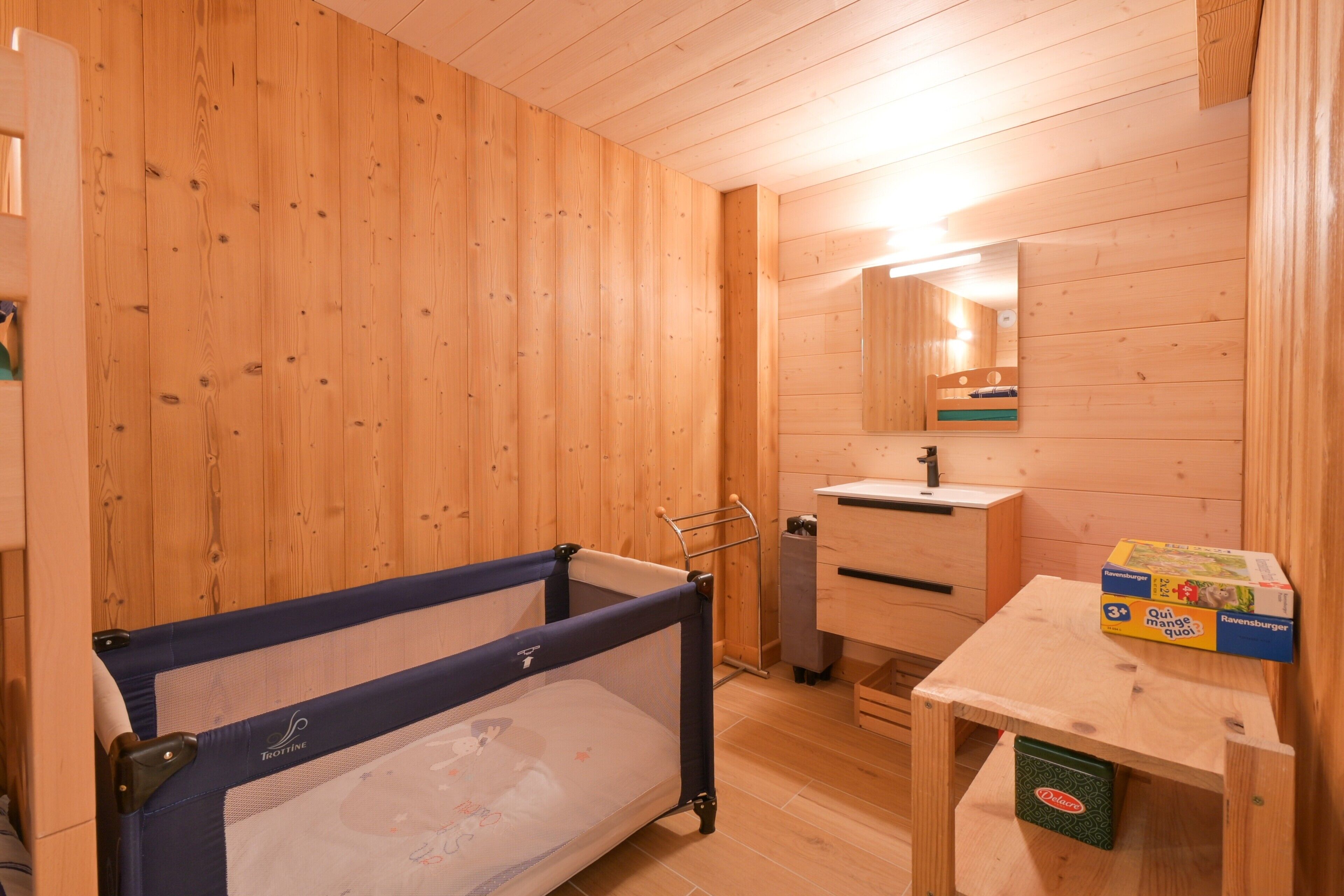 A wooden room with a crib, a small table, and a mirror.