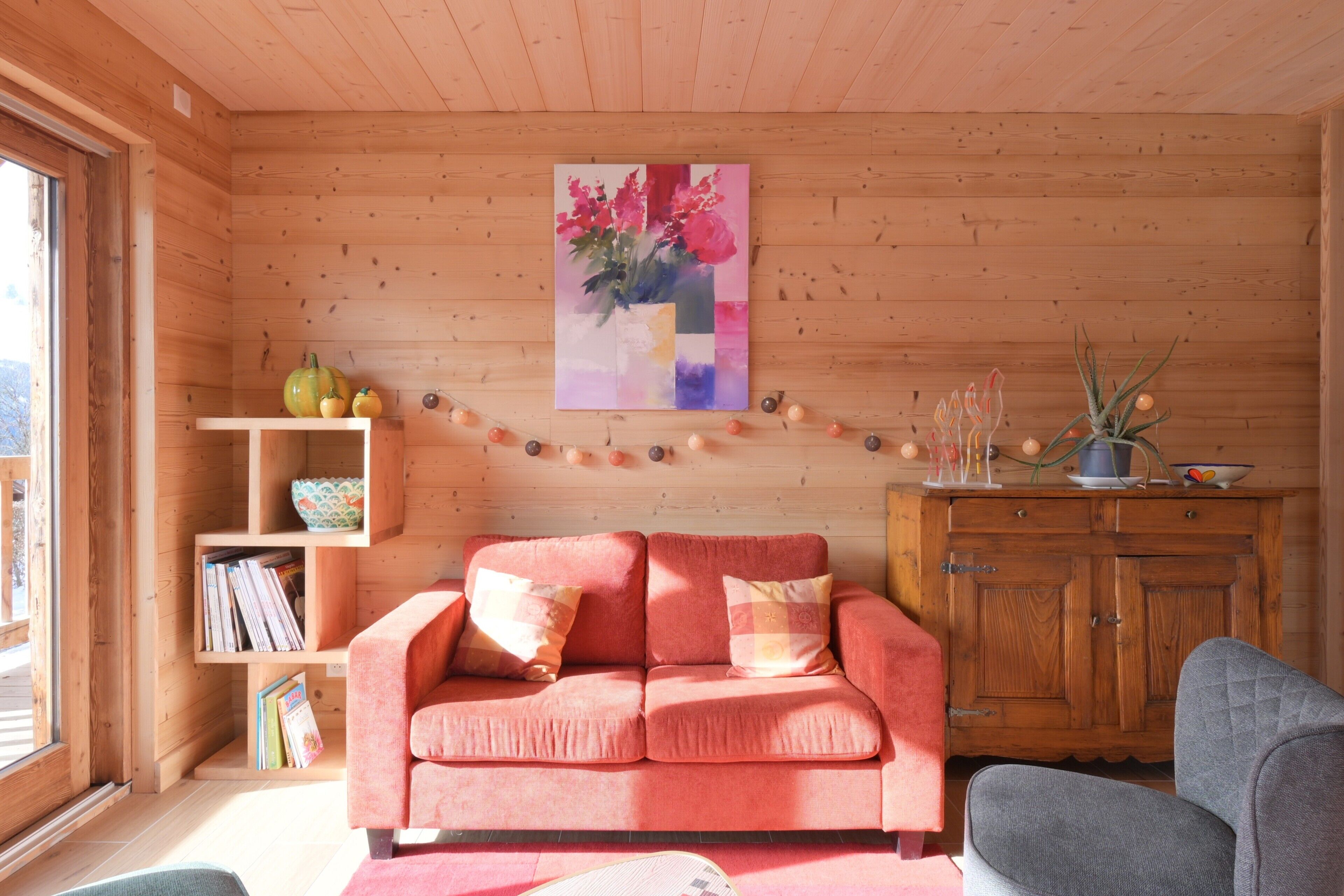 A wooden interior with a pink sofa, a bookshelf, and a wooden cabinet.