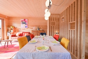 A wooden interior with a dining table set for six, chairs, a sofa, and a small kitchen area. - Apartment in Chalet L'Albert with Mountain View, Balcony, and Private Terrace (Manigod)