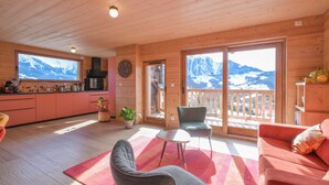 A wooden interior with a kitchen, seating area, and large windows with mountain views.