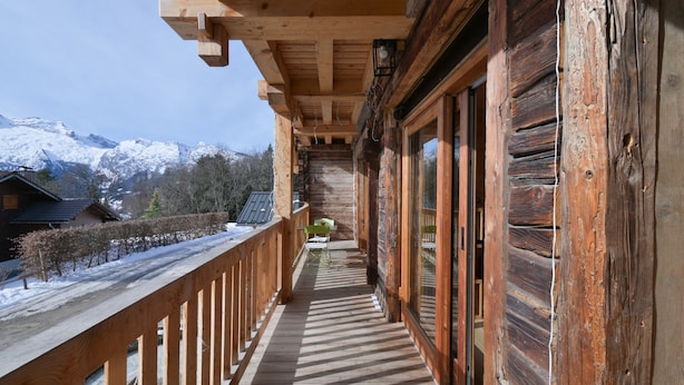 A wooden balcony with a view of snow-capped mountains, wooden railings, and a clear sky.