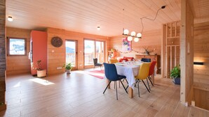 A wooden interior with a dining area, potted plants, and a view through the windows.