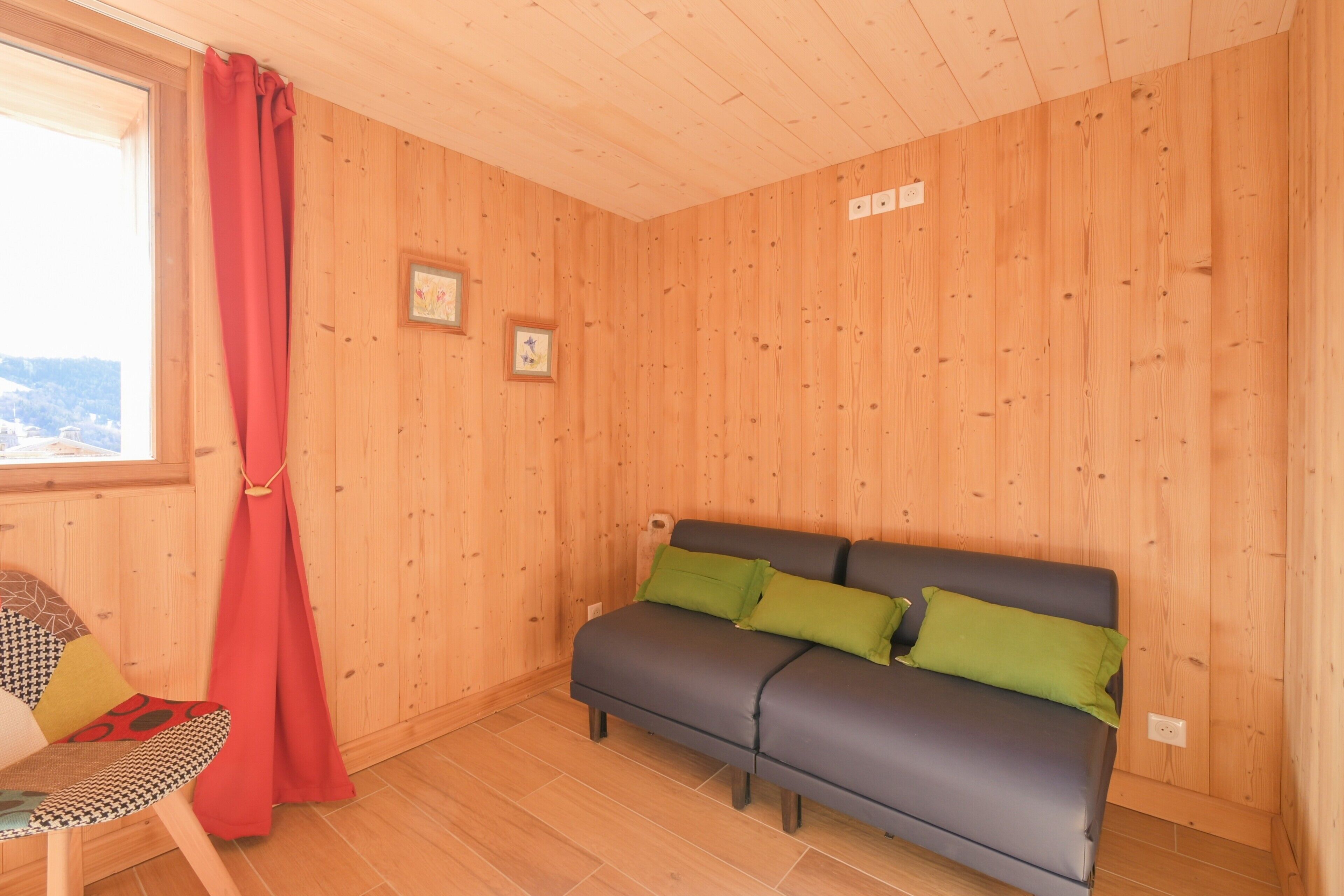 Una habitación con paneles de madera, un sofá, una silla y una ventana con cortinas rojas.
