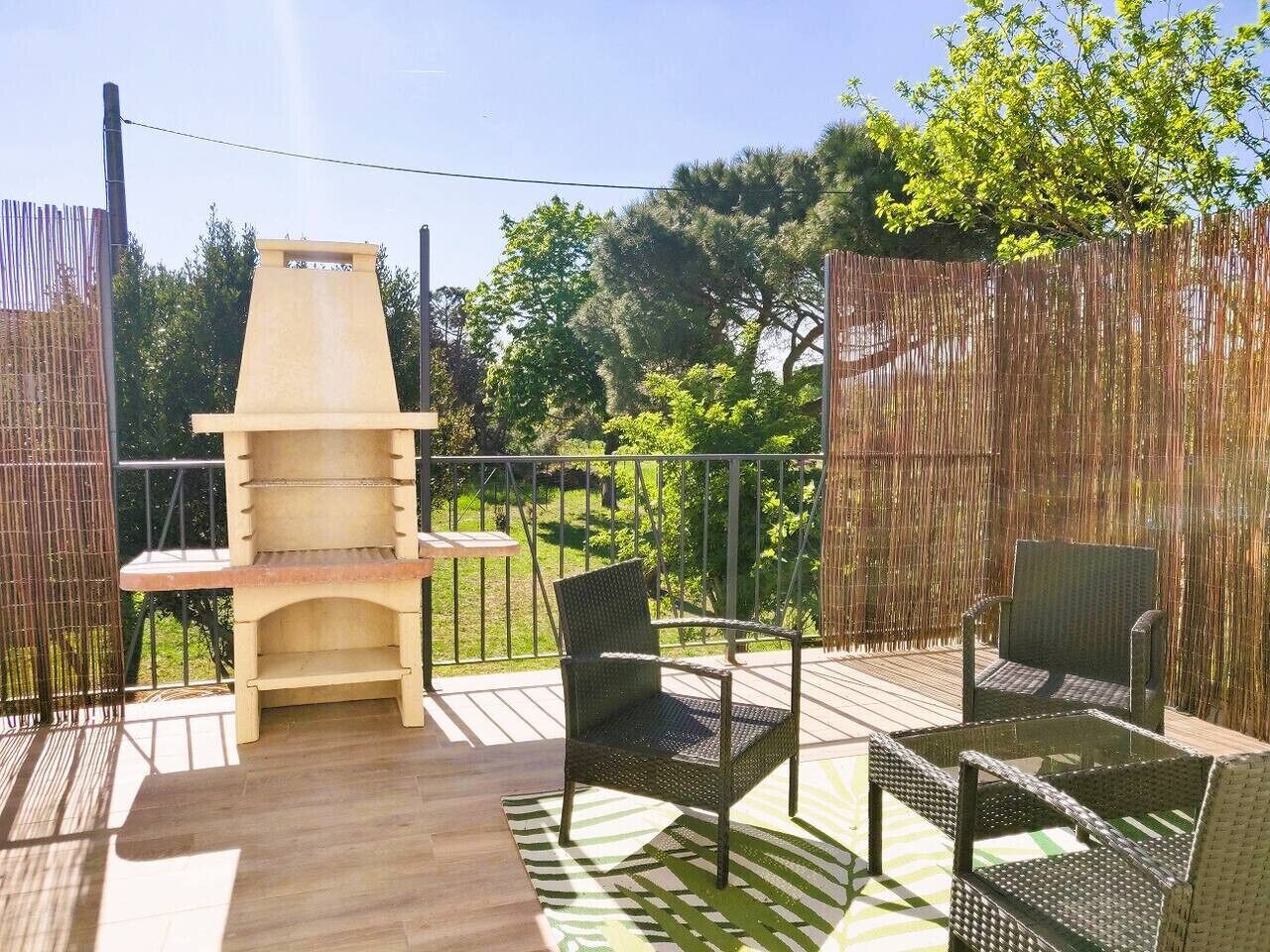 Un patio al aire libre con una parrilla, dos sillas de mimbre y una mesa.