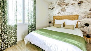 Een slaapkamer met een bakstenen muur, een houten hoofdbord, een bed met witte beddengoed en een groene plaid.