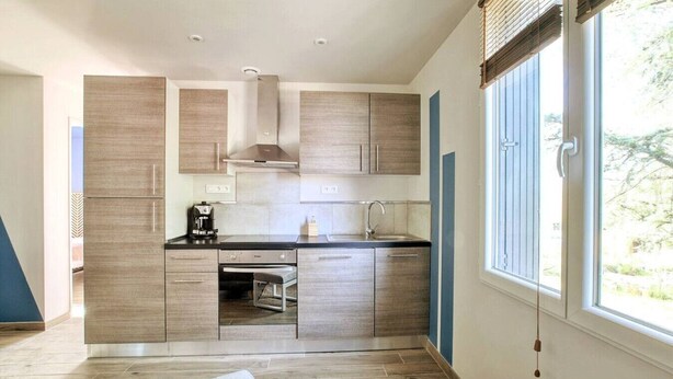 Een moderne keuken met houten kastjes, een inbouwoven en een raam met zonwering.