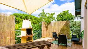 Een terras buiten met een houten tafel, stoelen, een barbecue en een bamboehek.