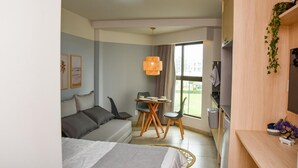 Ett modernt hotellrum med en säng, en soffa, ett matbord med stolar, en TV och ett stort fönster med utsikt över omgivningarna.