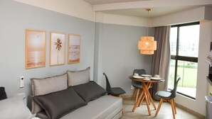 Ett modernt hotellrum med en grå soffa, ett matbord med stolar, en hängande lampa och inramade konstverk på väggen.