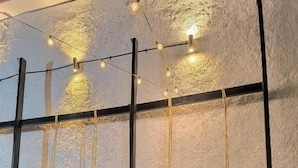 A ping pong table with two people playing, surrounded by a stone wall and hanging lights. - Haku Hostel Cusco (Cusco)