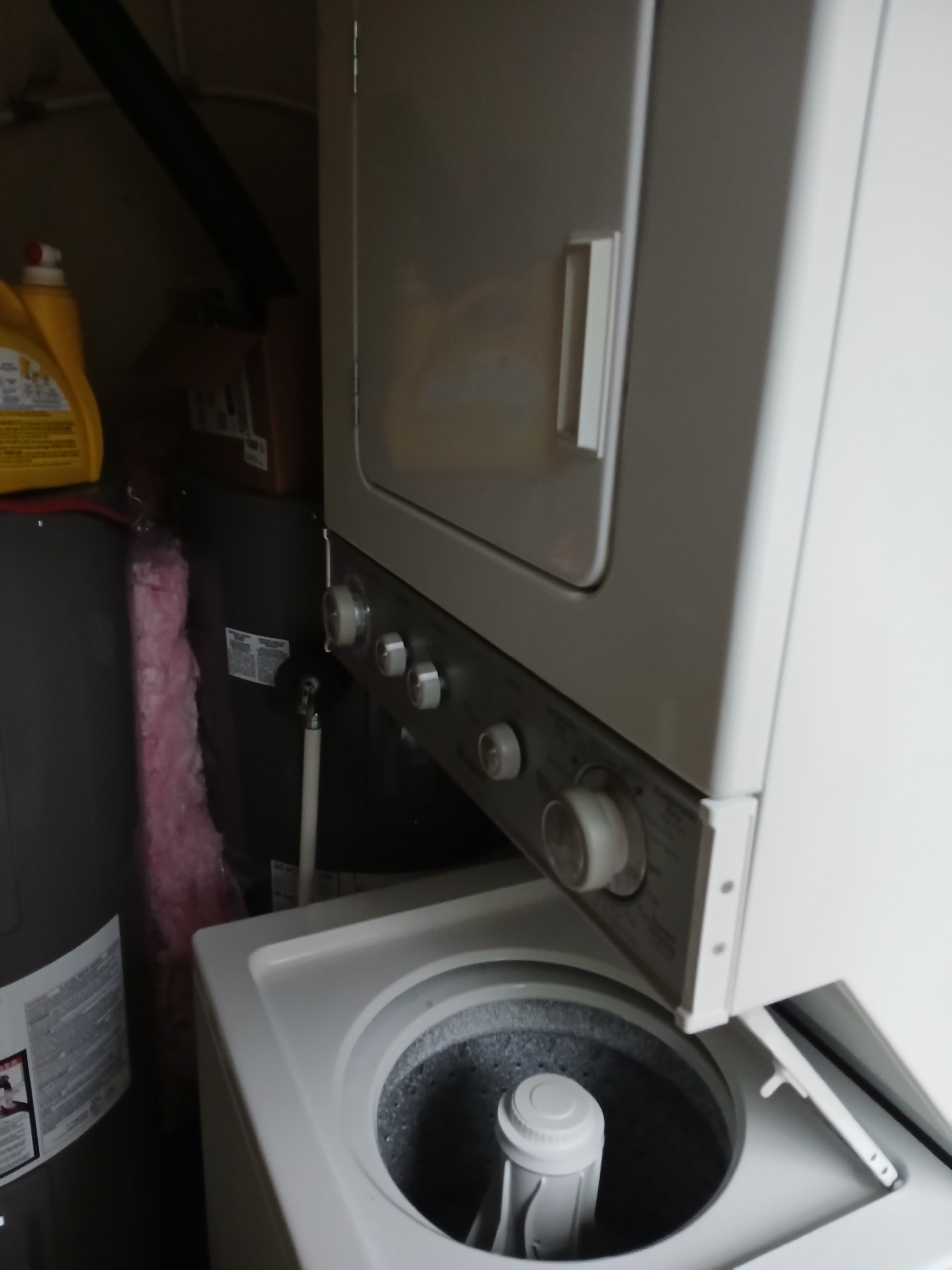 Ein kleiner, industrie-inspirierter Waschraum mit einer Waschmaschine mit Frontlader, einem großen Warmwasserspeicher und einer gelben Flasche Waschmittel.